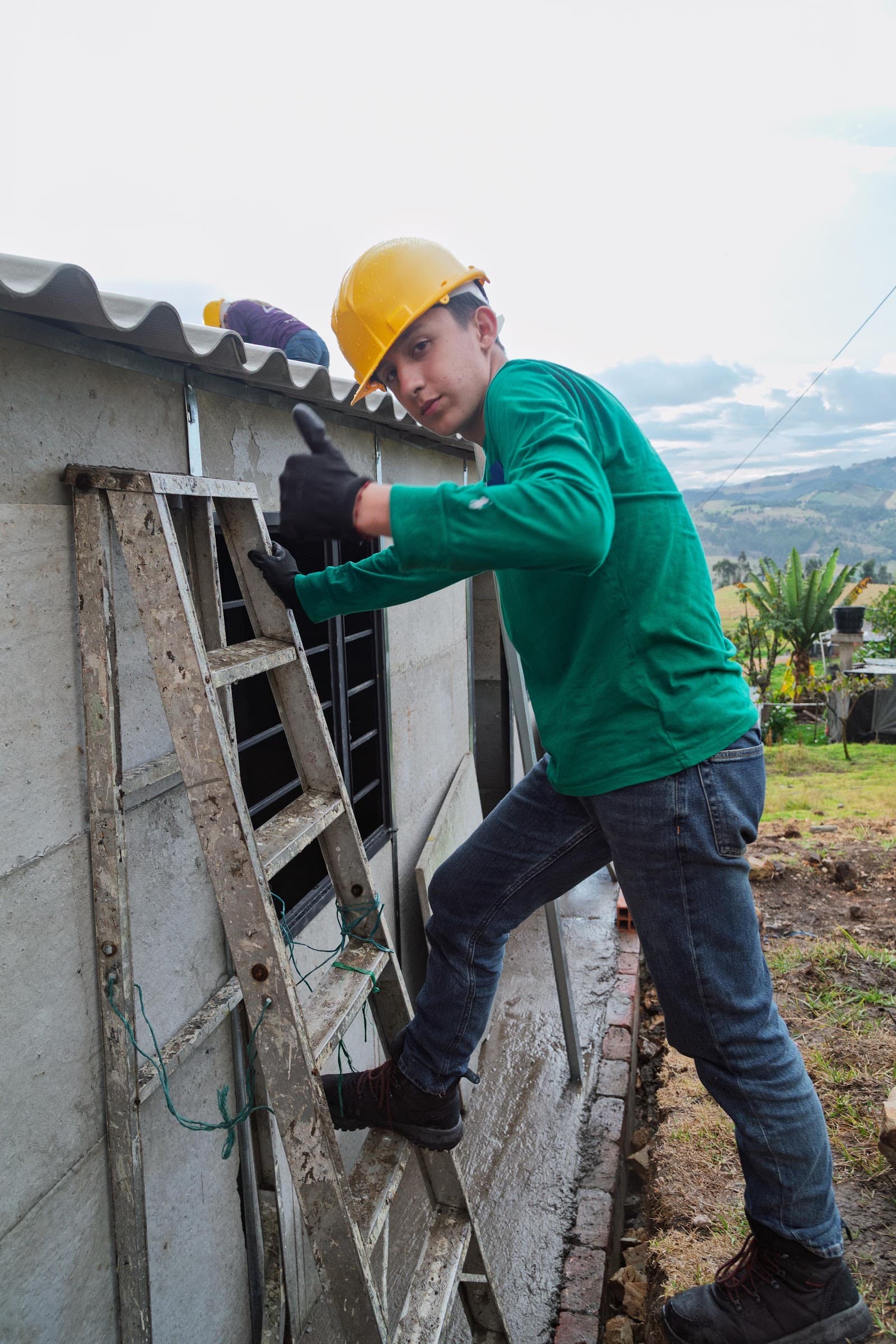 A young volunteer in a hard hat climbing a ladder while building a home in the Colombian Andes